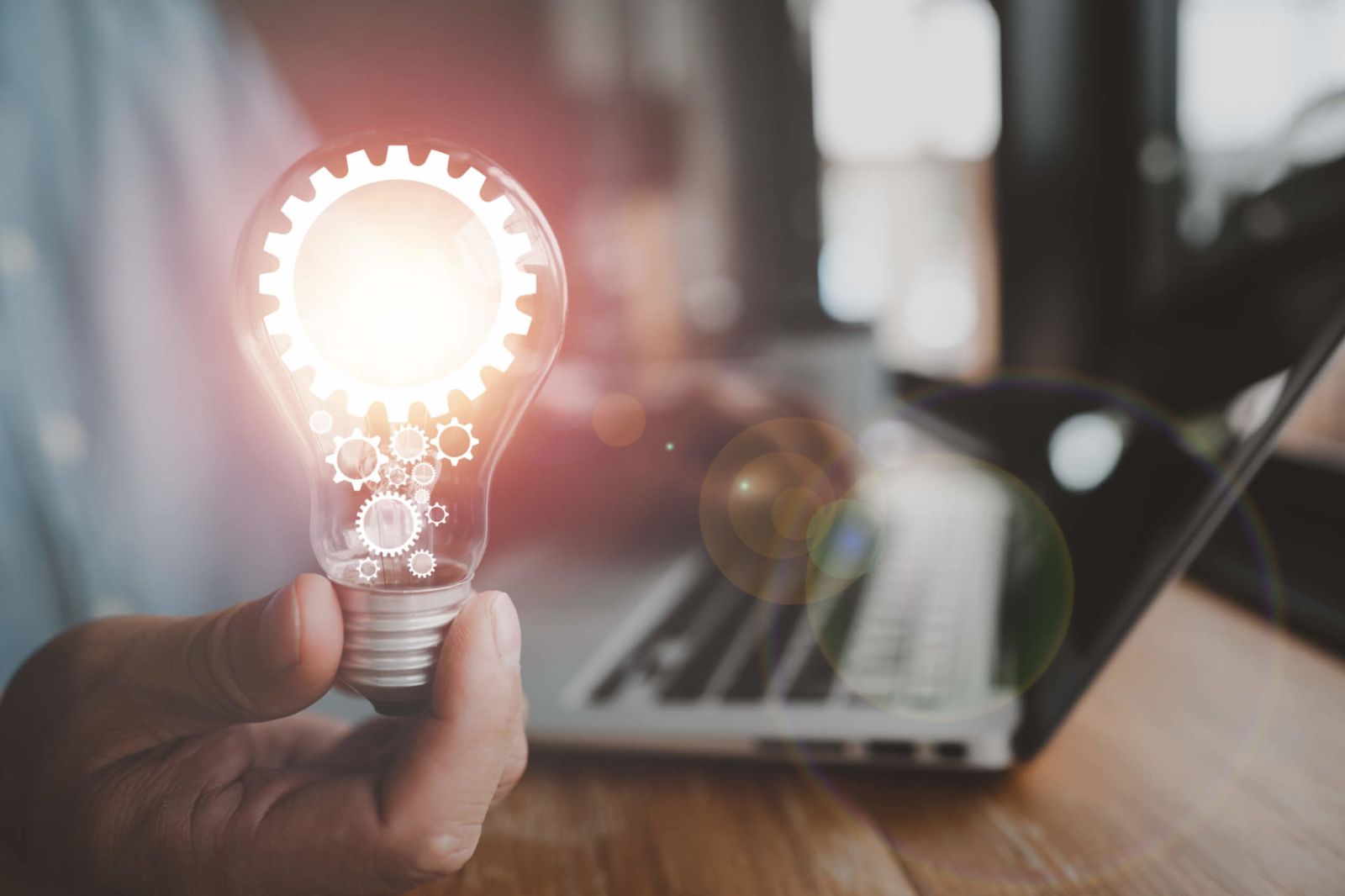 Close-up of a person typing on a laptop and also holding a bright lightbulb.