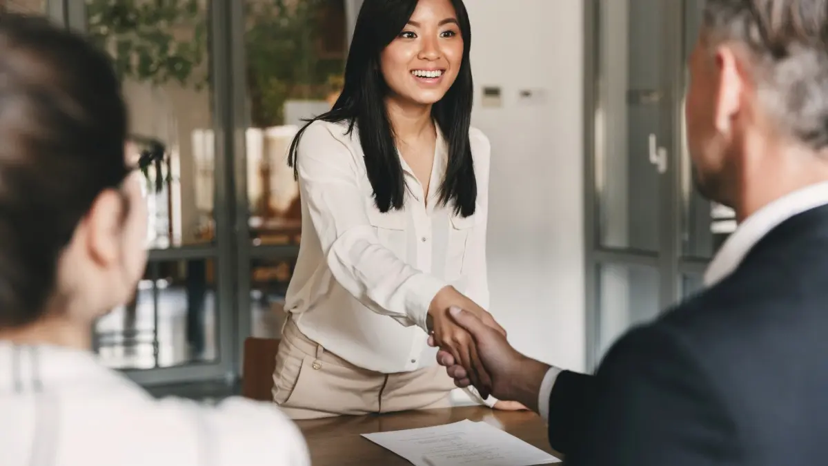 A job candidate shaking the hand of a hiring manager while smiling.